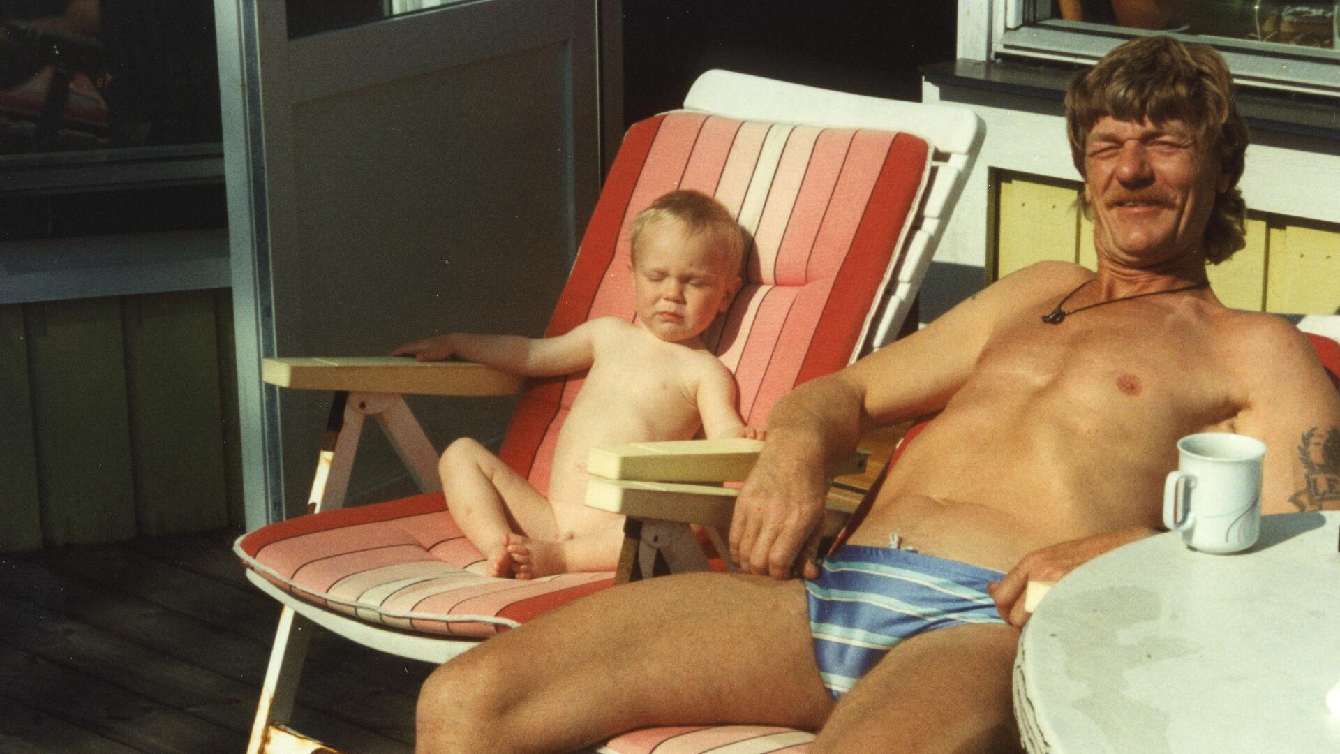 En man och ett litet barn i varsin solstol. Tittar in i kameran.