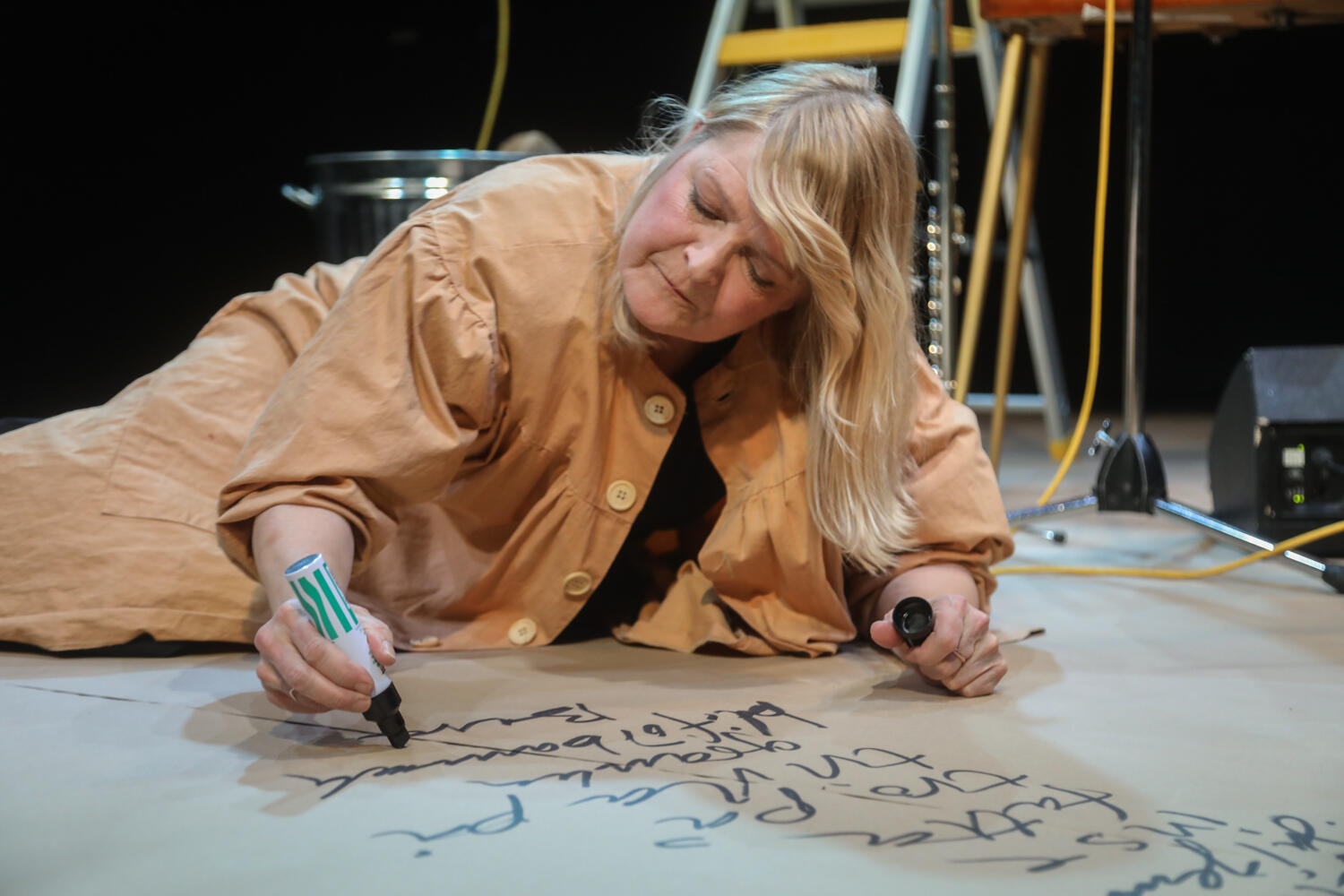 Åsa Gustafsson på scen, ligger på golvet och skriver på ett stort papper