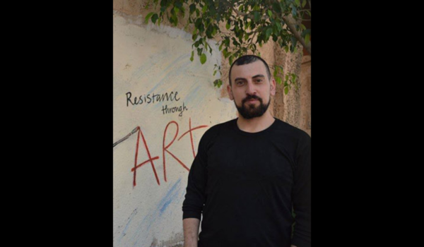 Ahmed Tobasi framför väggmålning med texten "Resistance through art"
